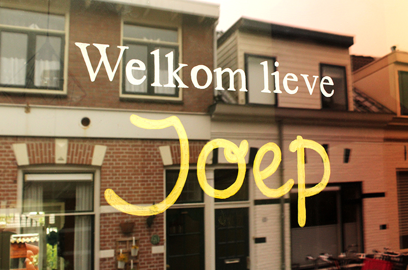 Huizen weerspiegeld in raam. Raamtekening met tekst "Welkom lieve Joep"